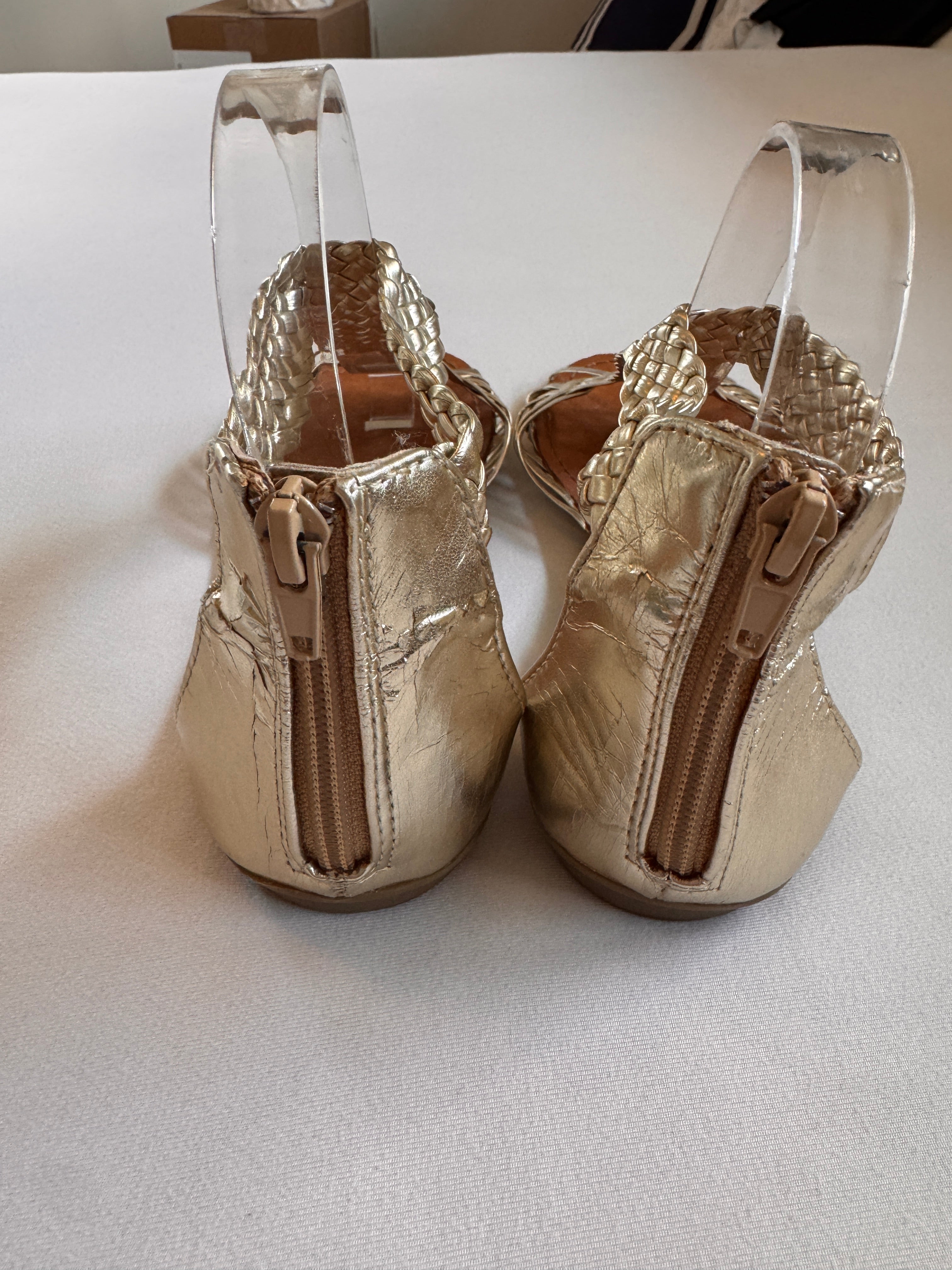 Pair of gold sandals shown from the back to feature the zip closure