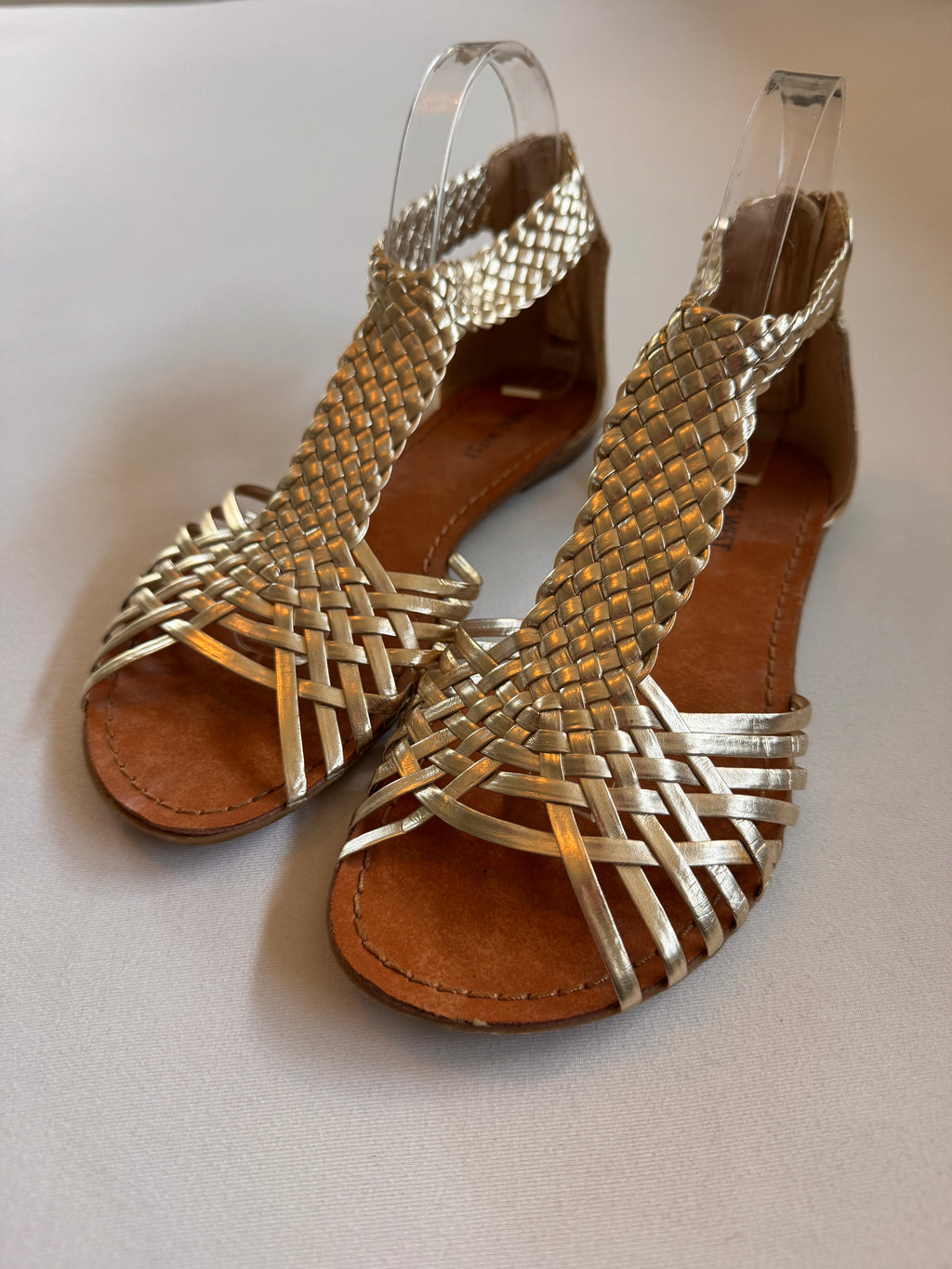 A pair of gold woven leather sandals on a white background