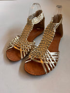 A pair of gold woven leather sandals on a white background