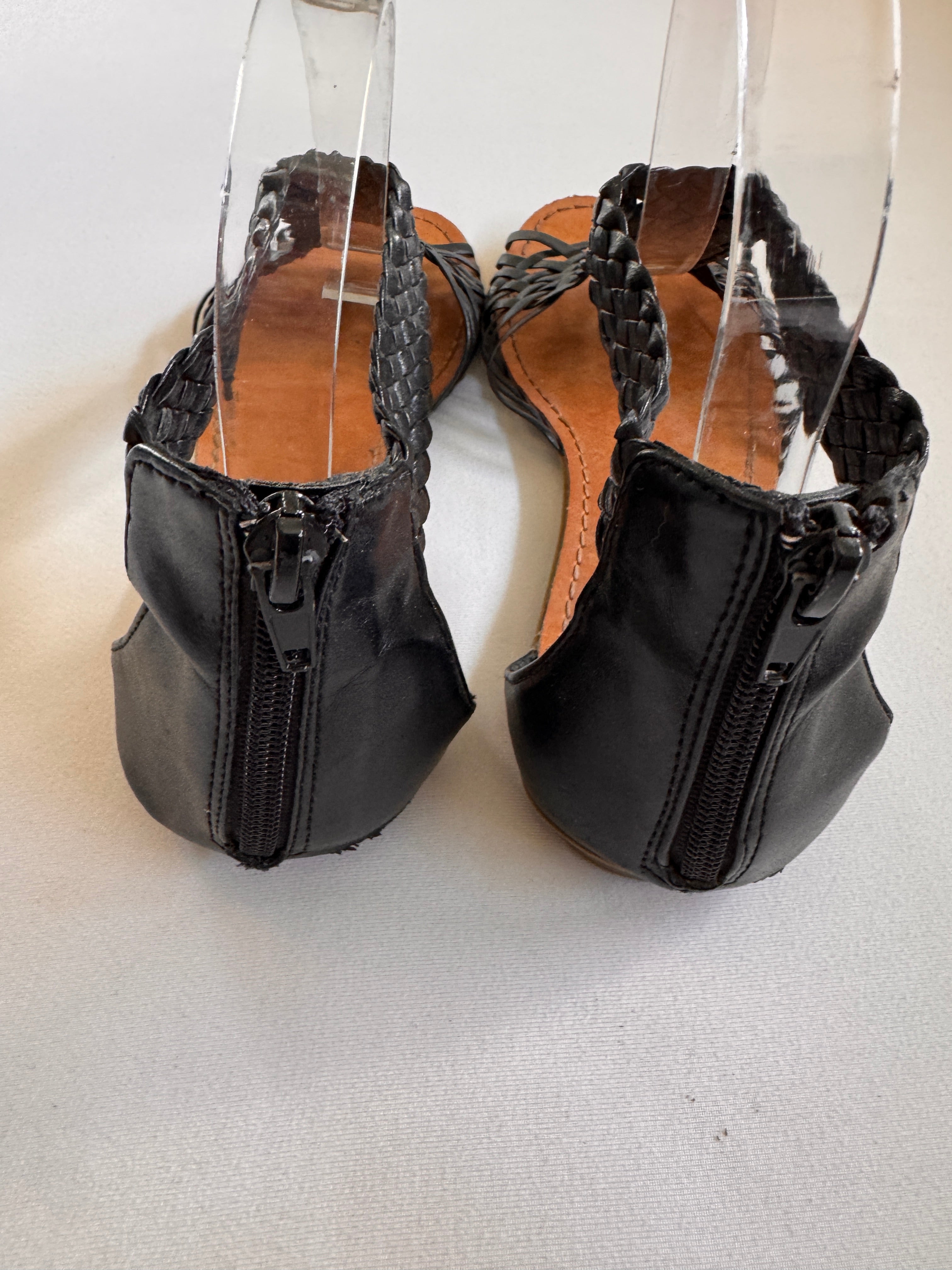 Back of black sandals showing a zip back closure on a white background