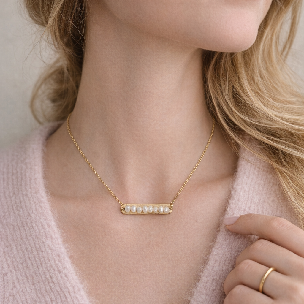 Gold necklace with pearls worn by a person, close-up on neck and chest area.