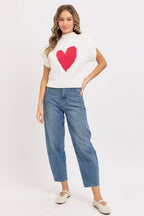 Woman wearing a white sweater with a red heart design and blue jeans on a white background