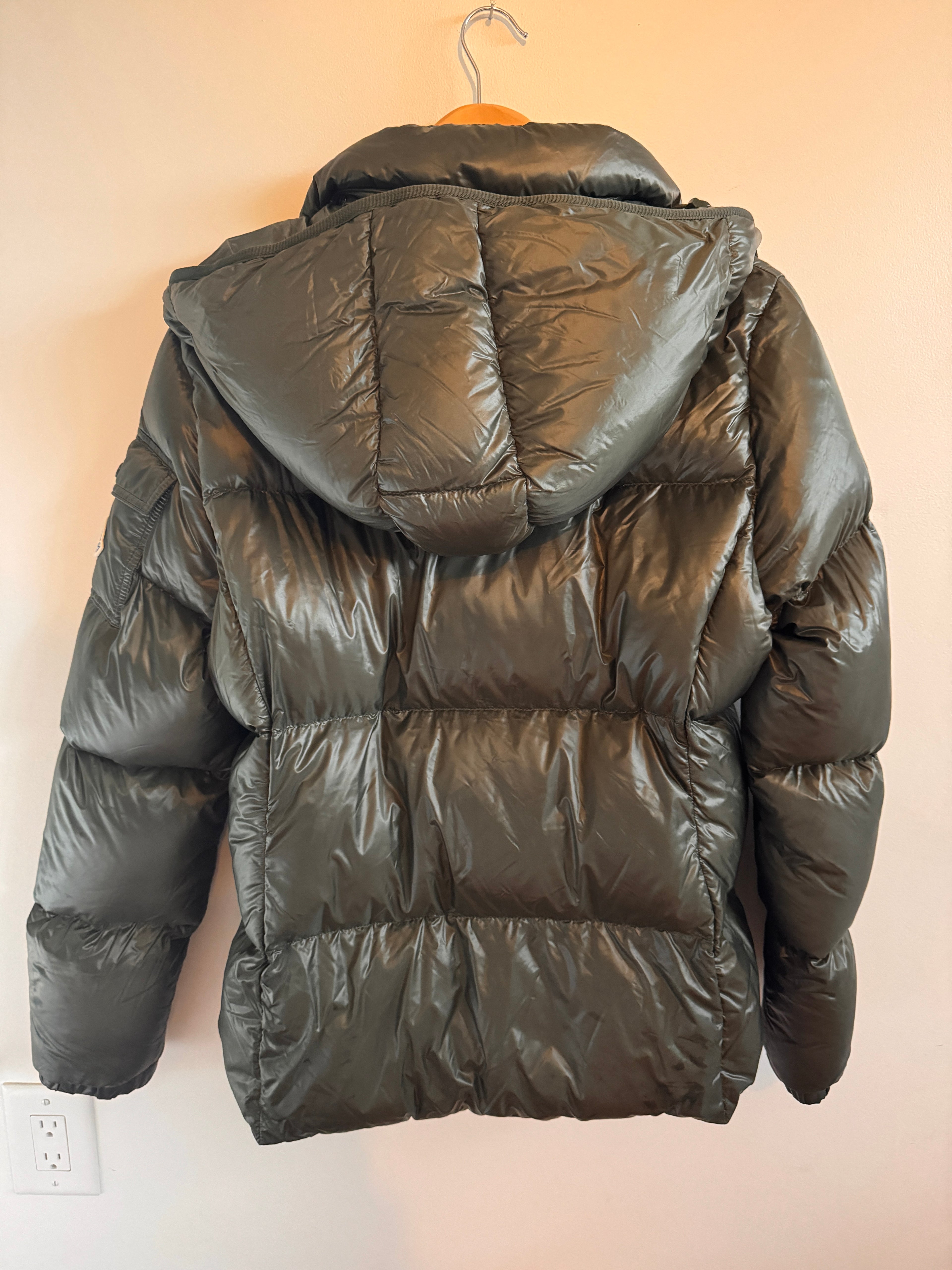 Dark green puffer jacket on a hanger against a beige wall.