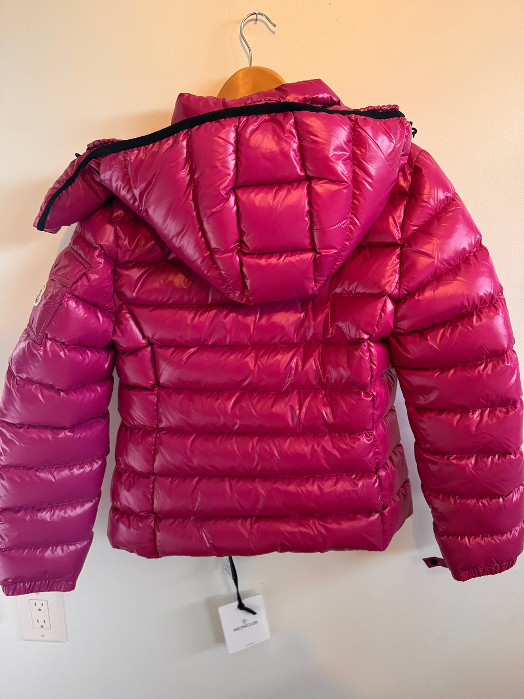 Pink puffer jacket  against a white wall.
