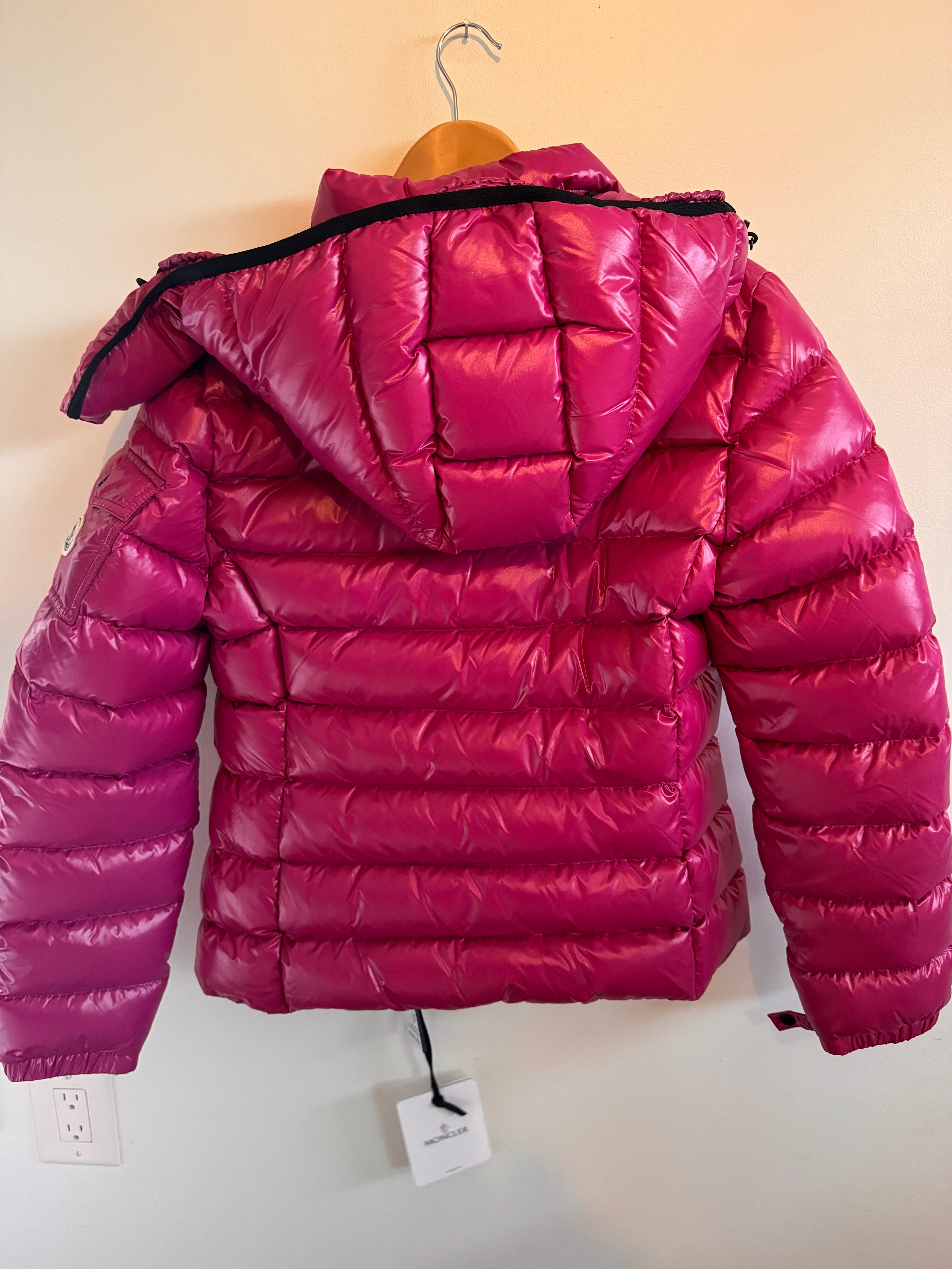 Pink puffer jacket  against a white wall.