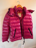 Pink puffer jacket on a hanger against a white wall