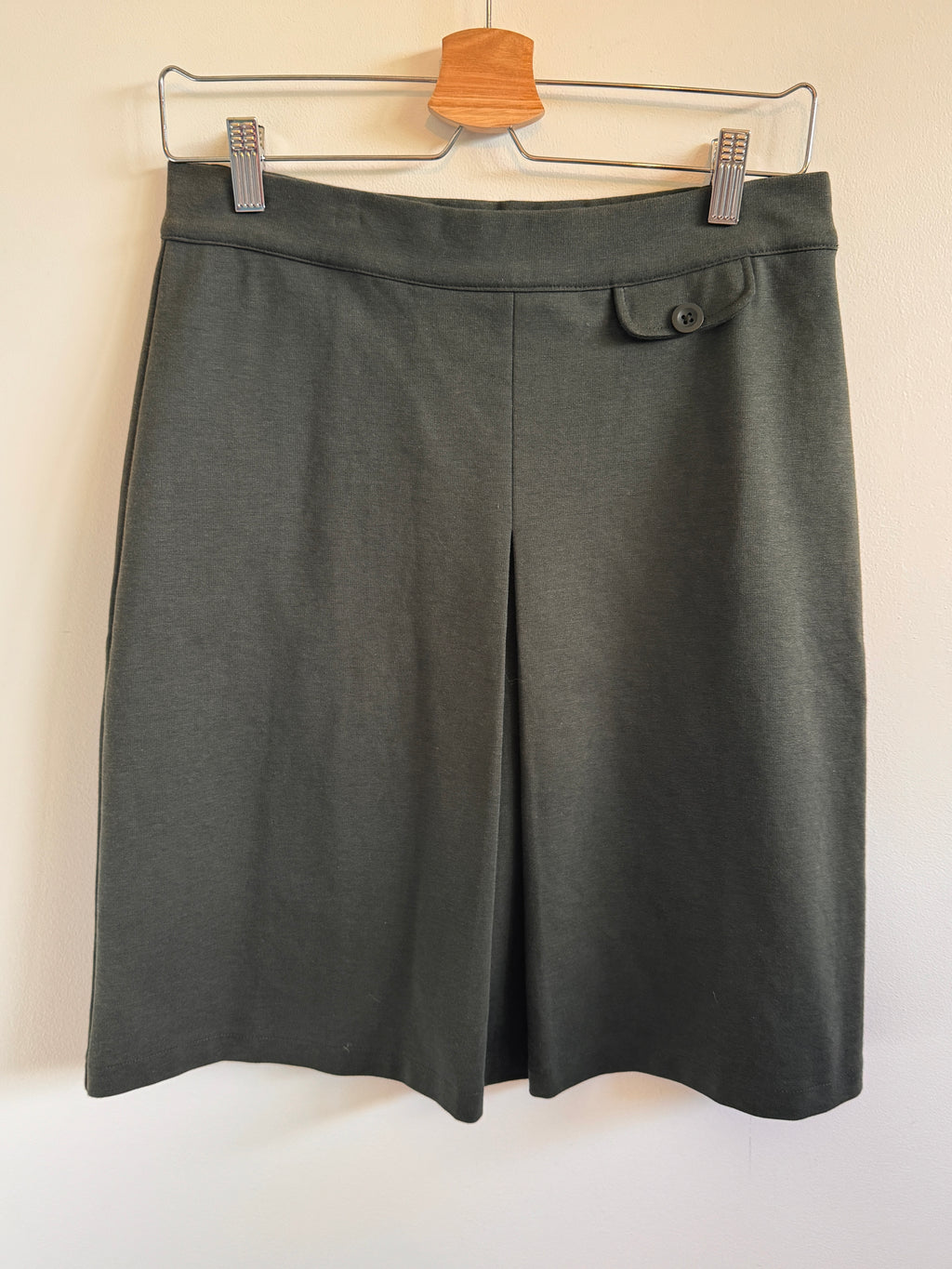 Dark olive skirt on a hanger against a plain background
