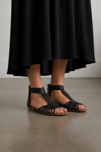 Person wearing black sandals and a black skirt on a plain background