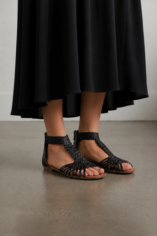Person wearing black sandals and a black skirt on a plain background
