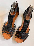 Black woven sandals with brown soles on a white background