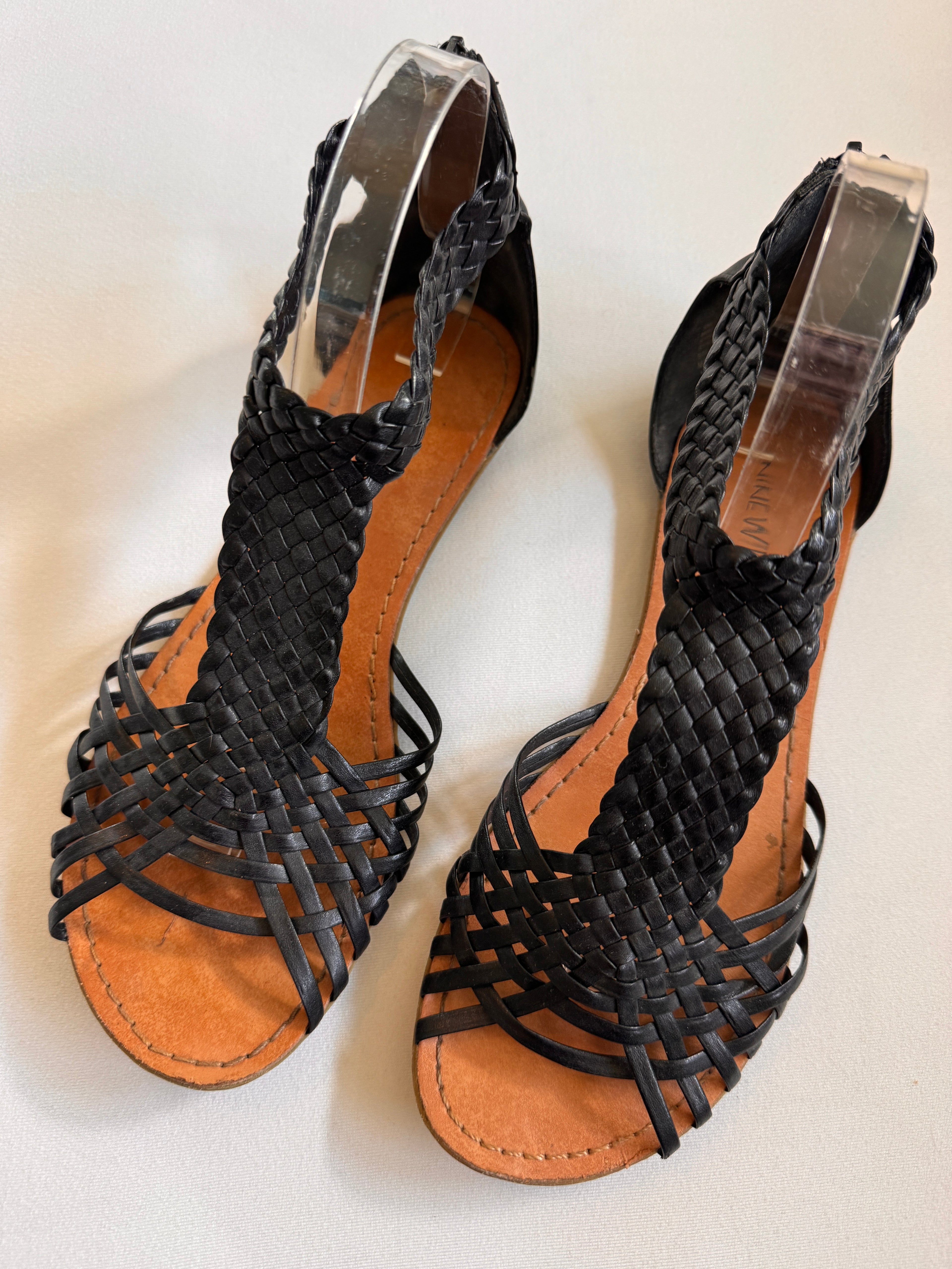 Black woven sandals with brown soles on a white background
