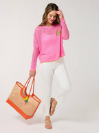 Woman wearing a pink sweater and white pants, holding an orange and brown bag on a white background