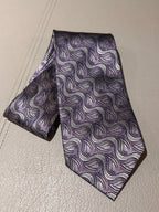 A patterned necktie with a purple, gray, and white wavy paisley design, laid flat on a light beige textured surface.