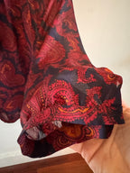 Red and black patterned fabric held by a hand against a neutral background