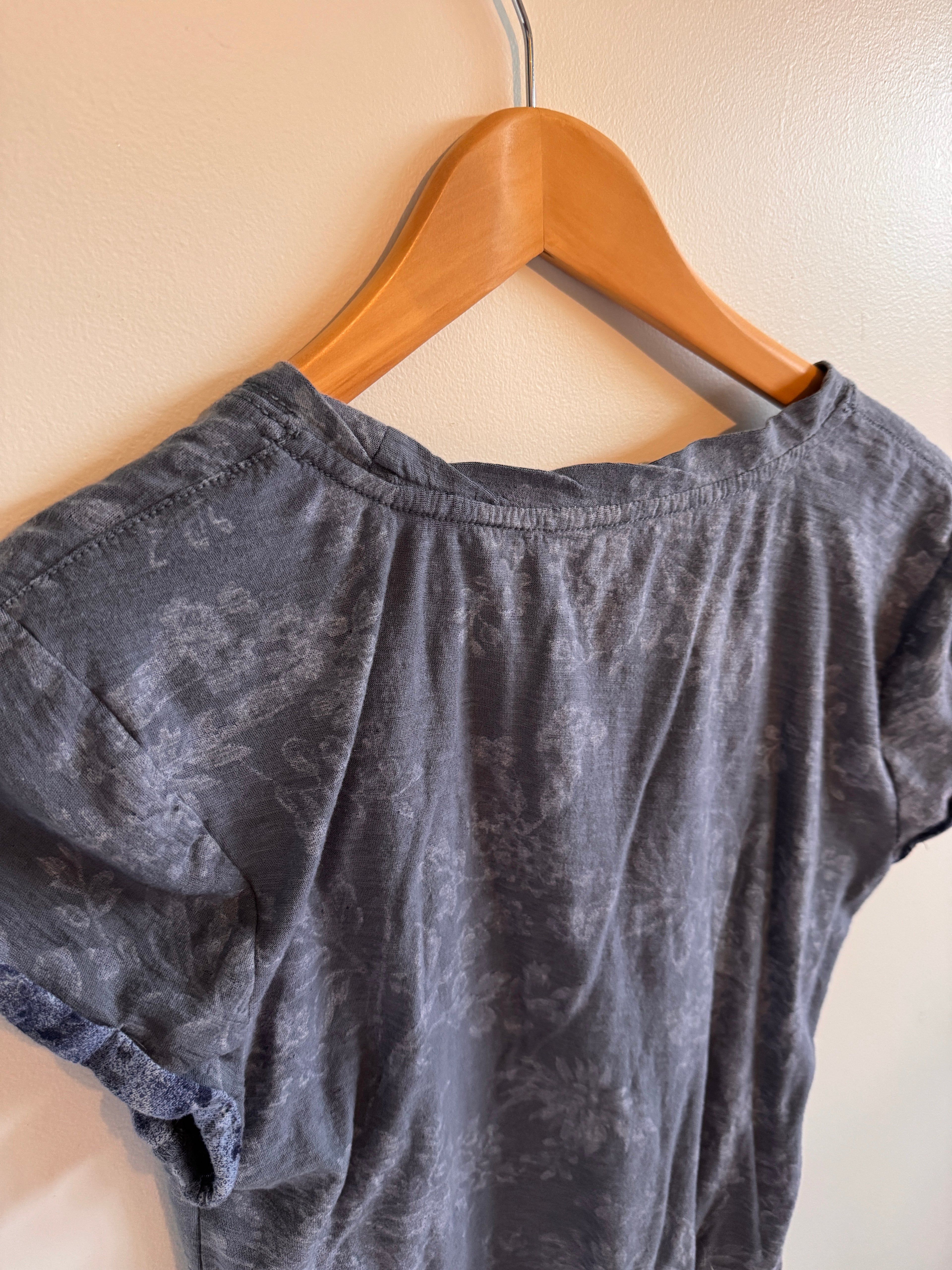 Blue floral top on a wooden hanger against a beige background