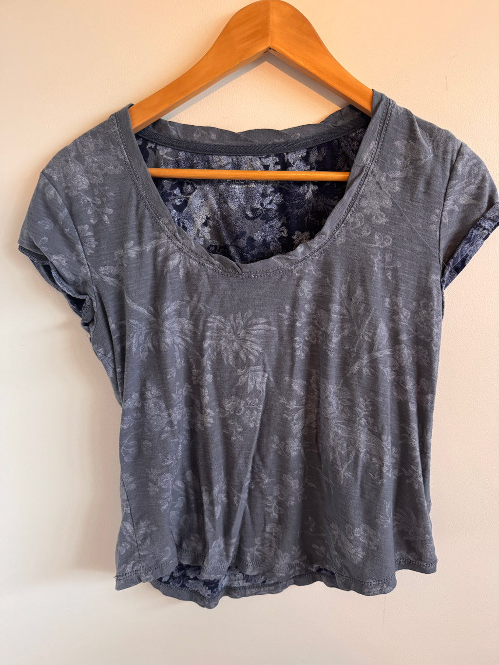 Blue textured shirt on a wooden hanger against a beige background
