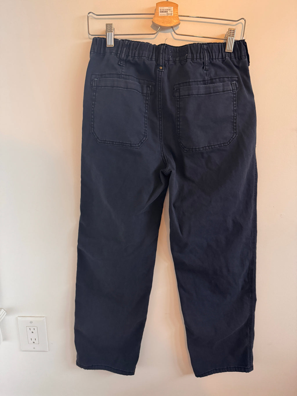 Folded navy blue pants on a beige surface with a wall outlet in the background.
