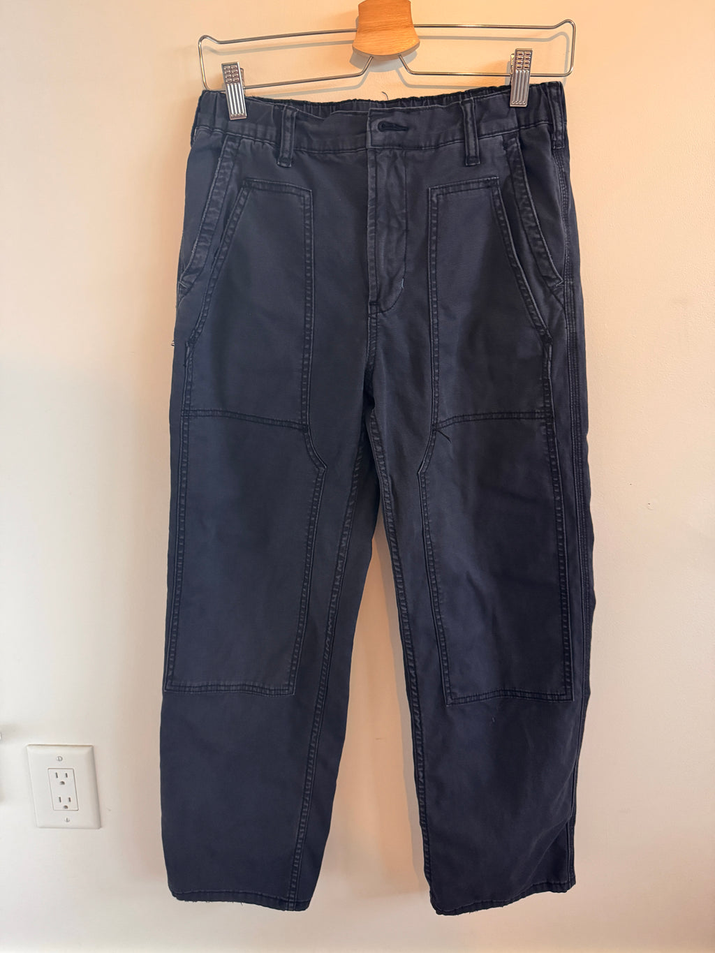 Folded navy blue pants on a wooden hanger against a beige wall.