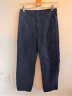 Folded navy blue pants on a wooden hanger against a beige wall.