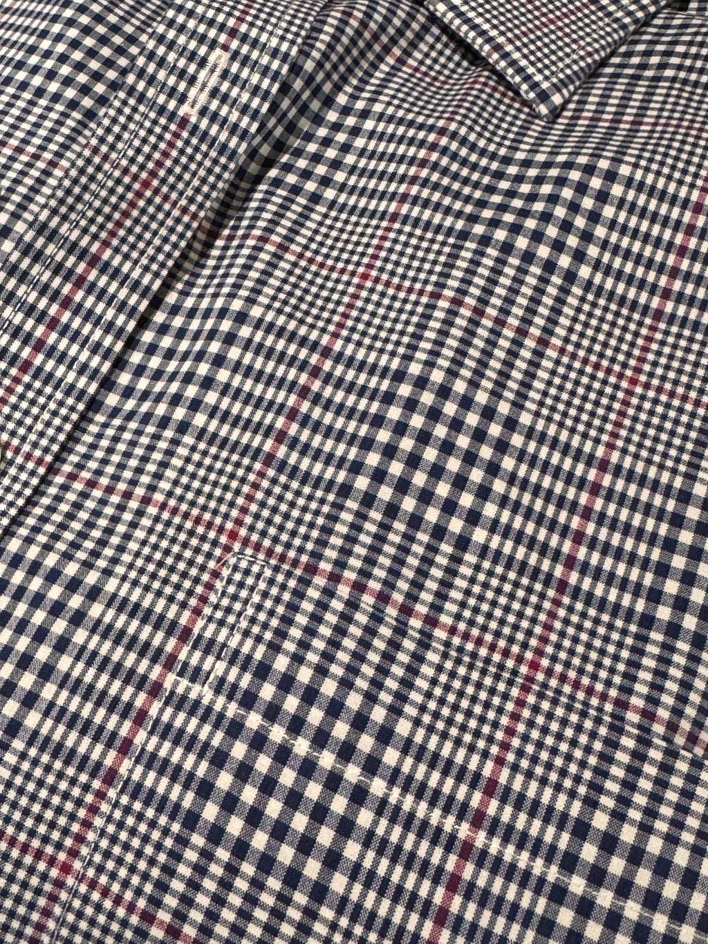 Close-up of a plaid shirt fabric with a navy blue and off-white gingham base and thin red overcheck lines.
