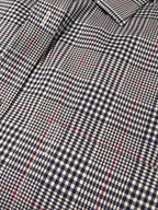 Close-up of a plaid shirt fabric with a navy blue and off-white gingham base and thin red overcheck lines.
