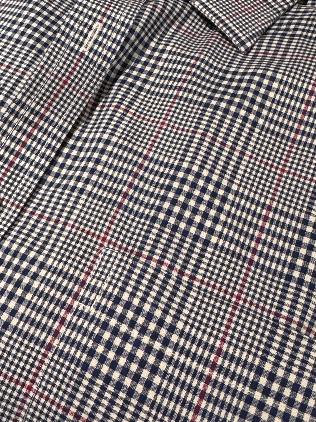 Close-up of a plaid shirt fabric with a navy blue and off-white gingham base and thin red overcheck lines.