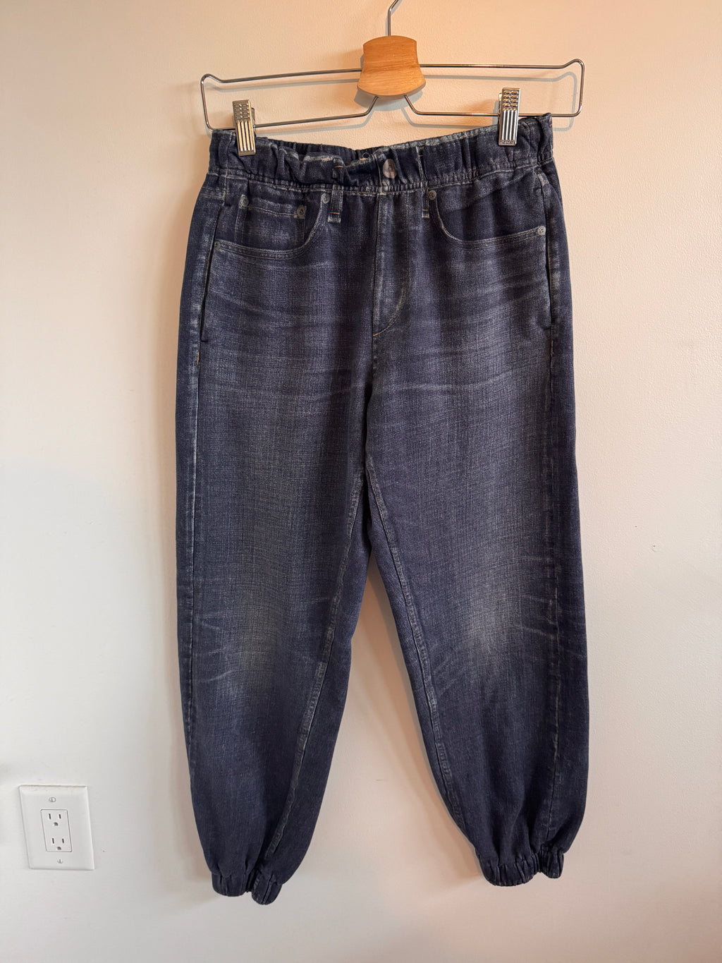 Pair of blue jeans on a hanger against a beige wall.