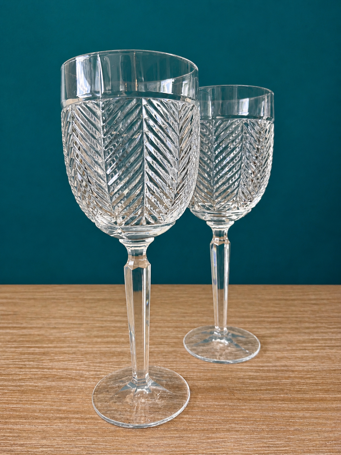 Two crystal wine glasses with intricate designs on a wooden surface and teal background