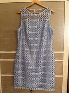 A sleeveless light blue lace dress with a scalloped hem and geometric floral lace pattern, hanging on a wooden hanger against a light wood drawer or cabinet background.