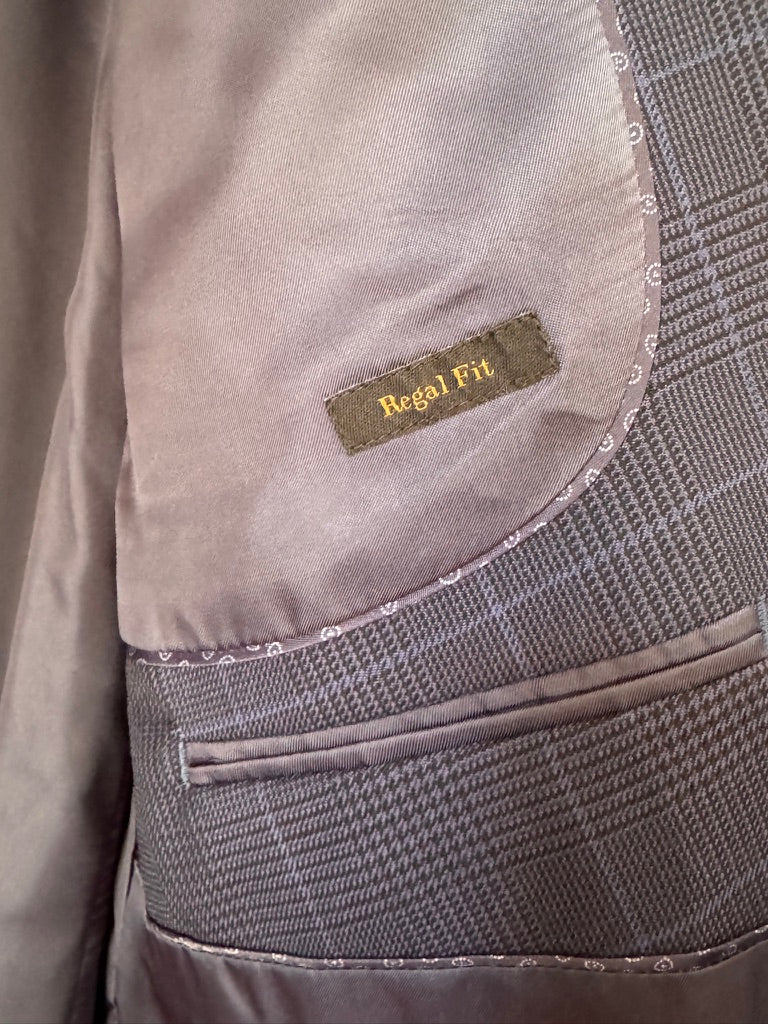 Close-up of a tailored jacket or blazer showing the interior lining, a small sewn label reading 'Regal Fit,' and a gray textured fabric pocket with stitched edges.