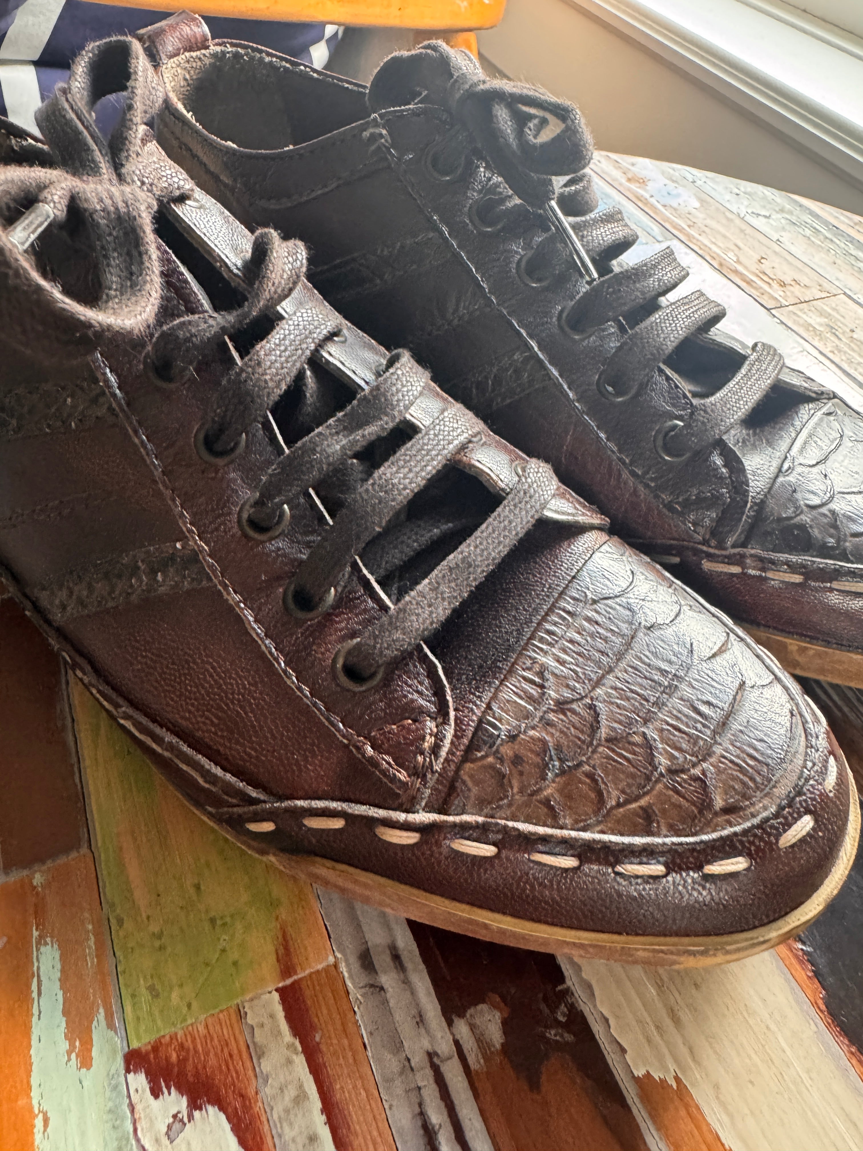 Brown leather sneakers with black laces on a wooden surface