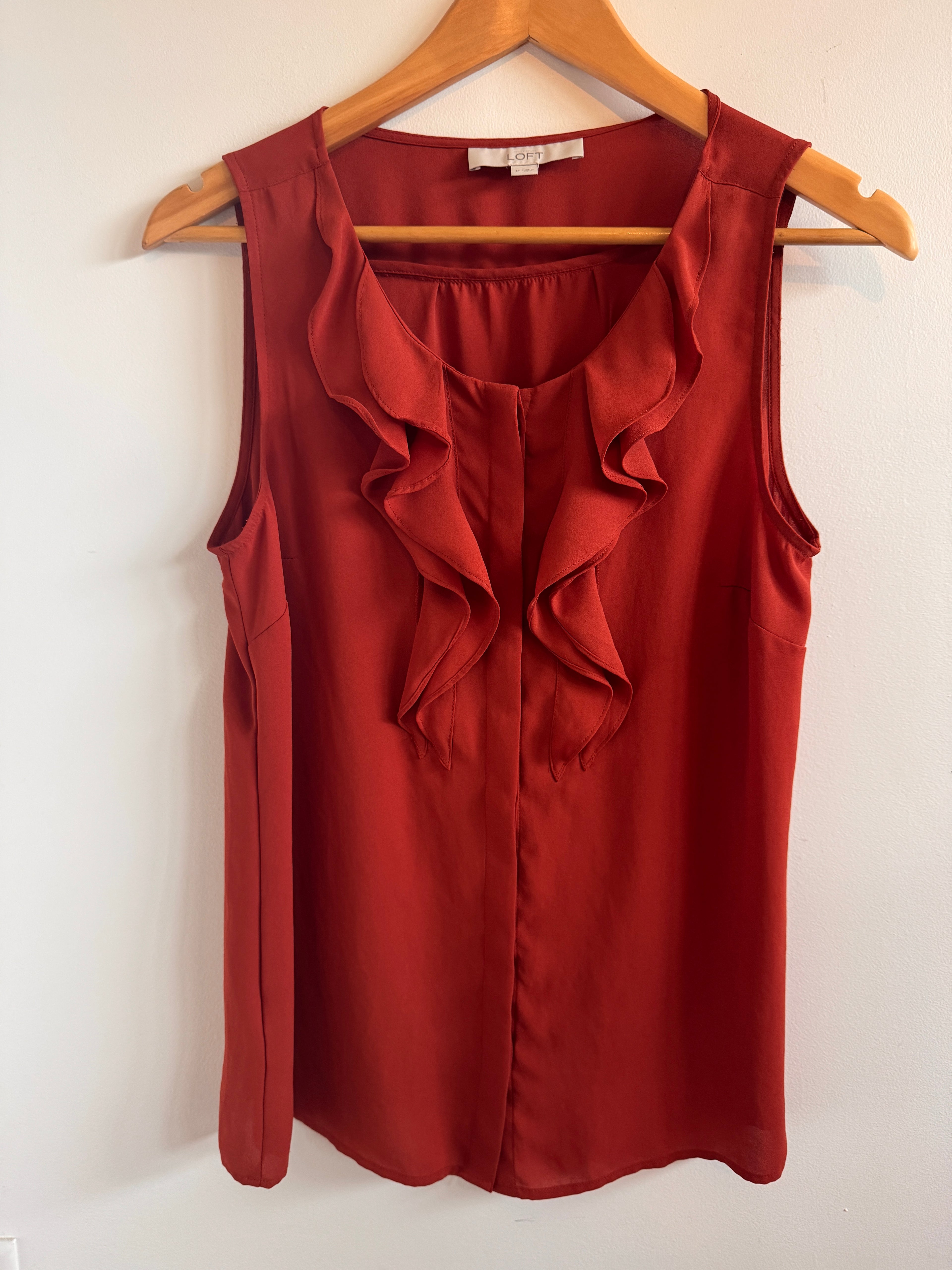 Rust colored top on a wooden hanger against a white background