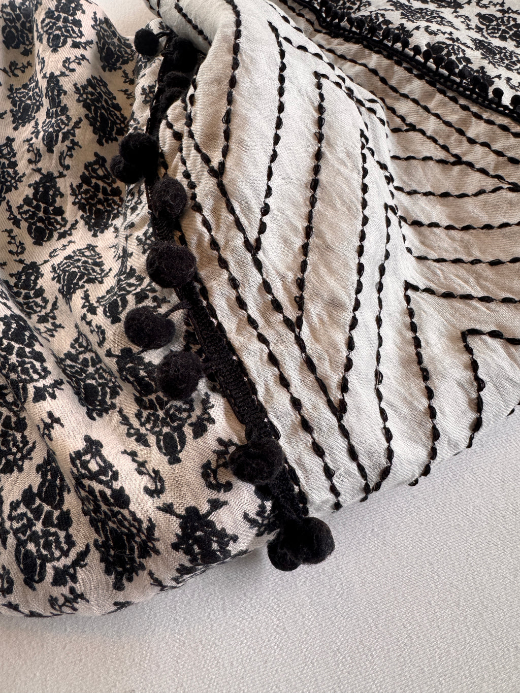 Textile with black floral pattern and black pom-poms on a neutral background