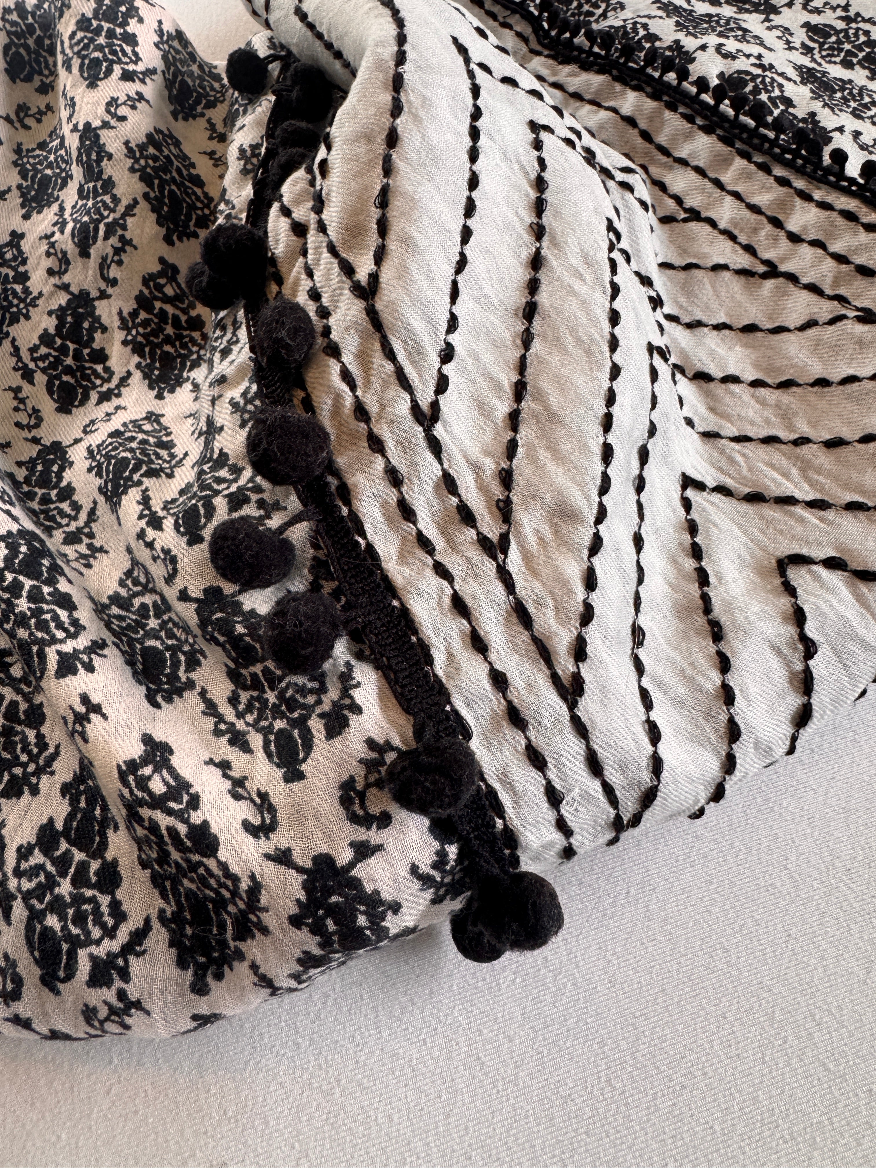 Textile with black floral pattern and black pom-poms on a neutral background
