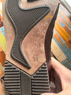 Close-up of a brown shoe sole with textured pattern and brand logo on a colorful wooden surface.