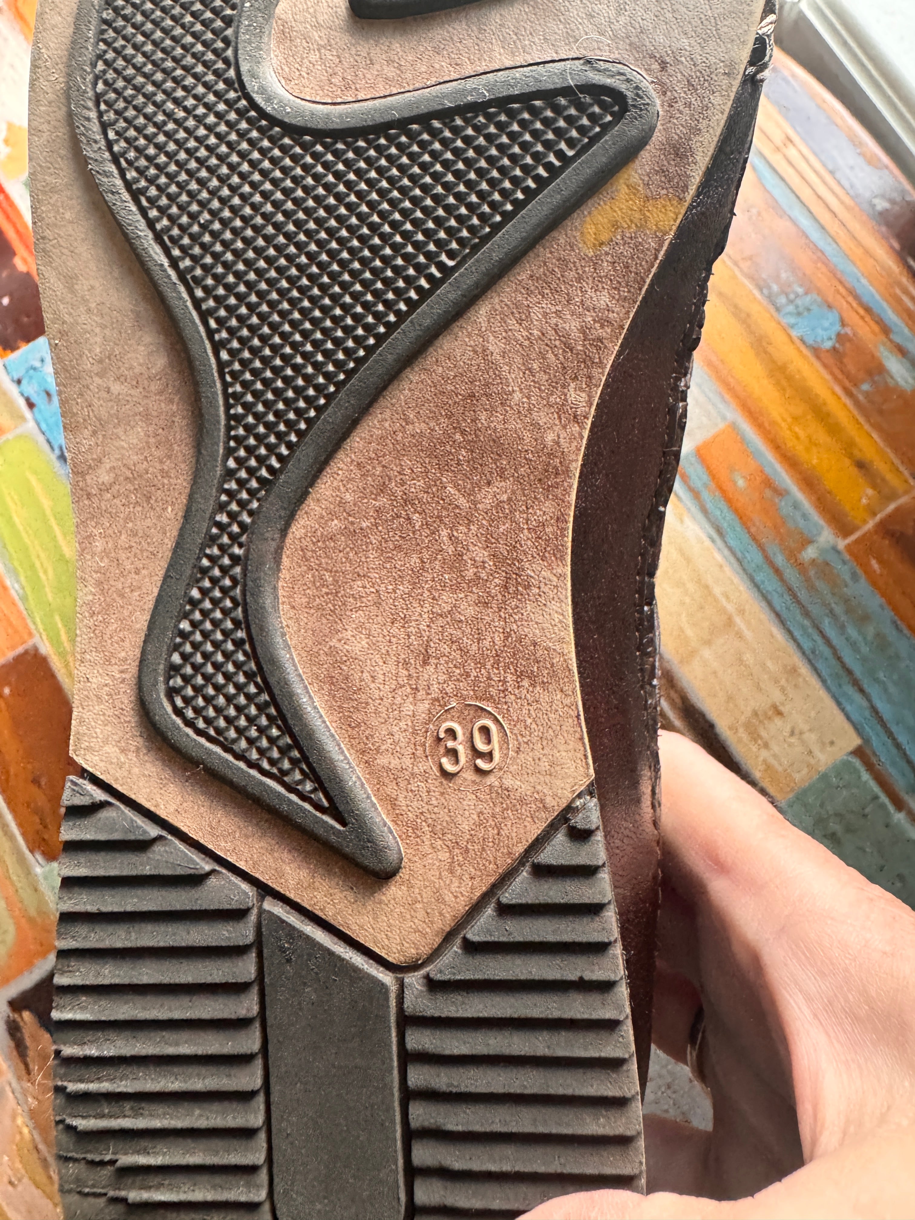 Close-up of a brown shoe sole with textured pattern and brand logo on a colorful wooden surface.
