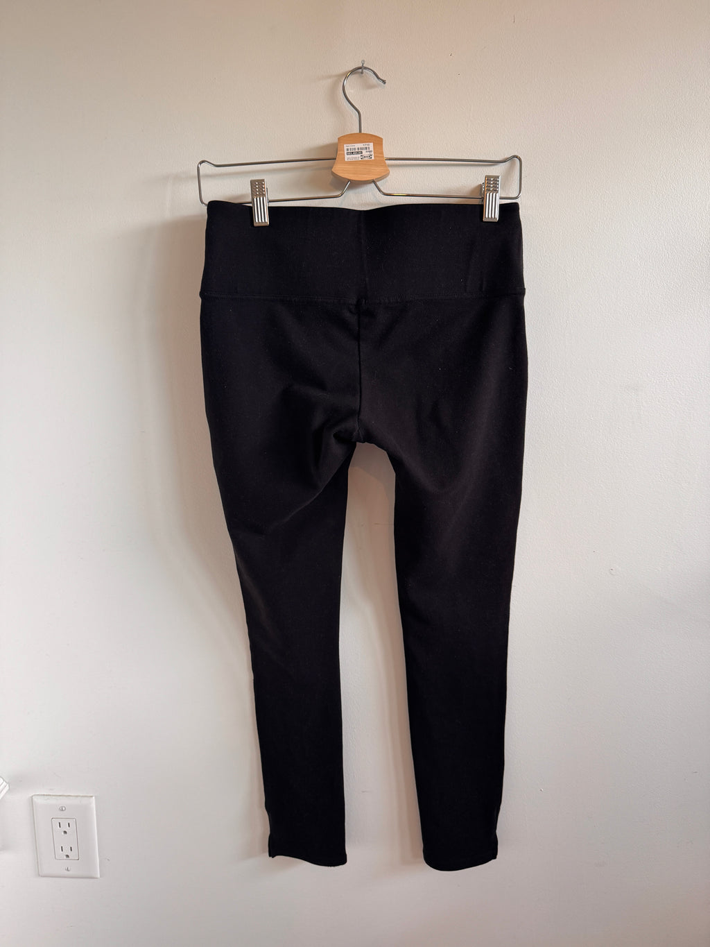 Black pants on a hanger against a white wall