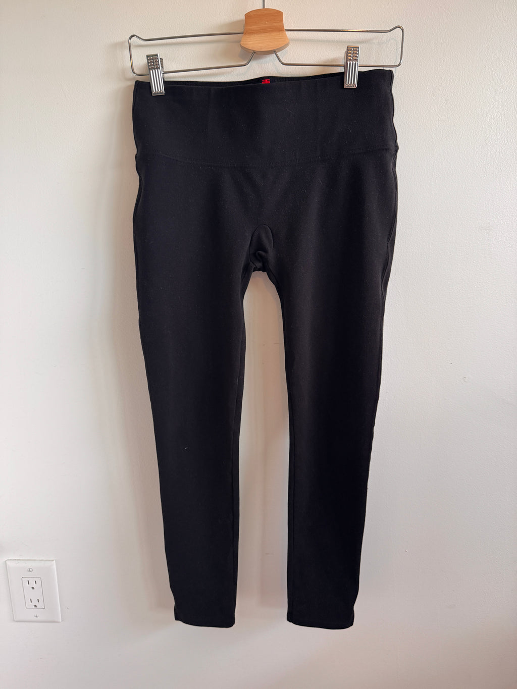 Black pants hanging on a white wall with a wooden hanger.