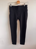 Black pants hanging on a white wall with a wooden hanger.
