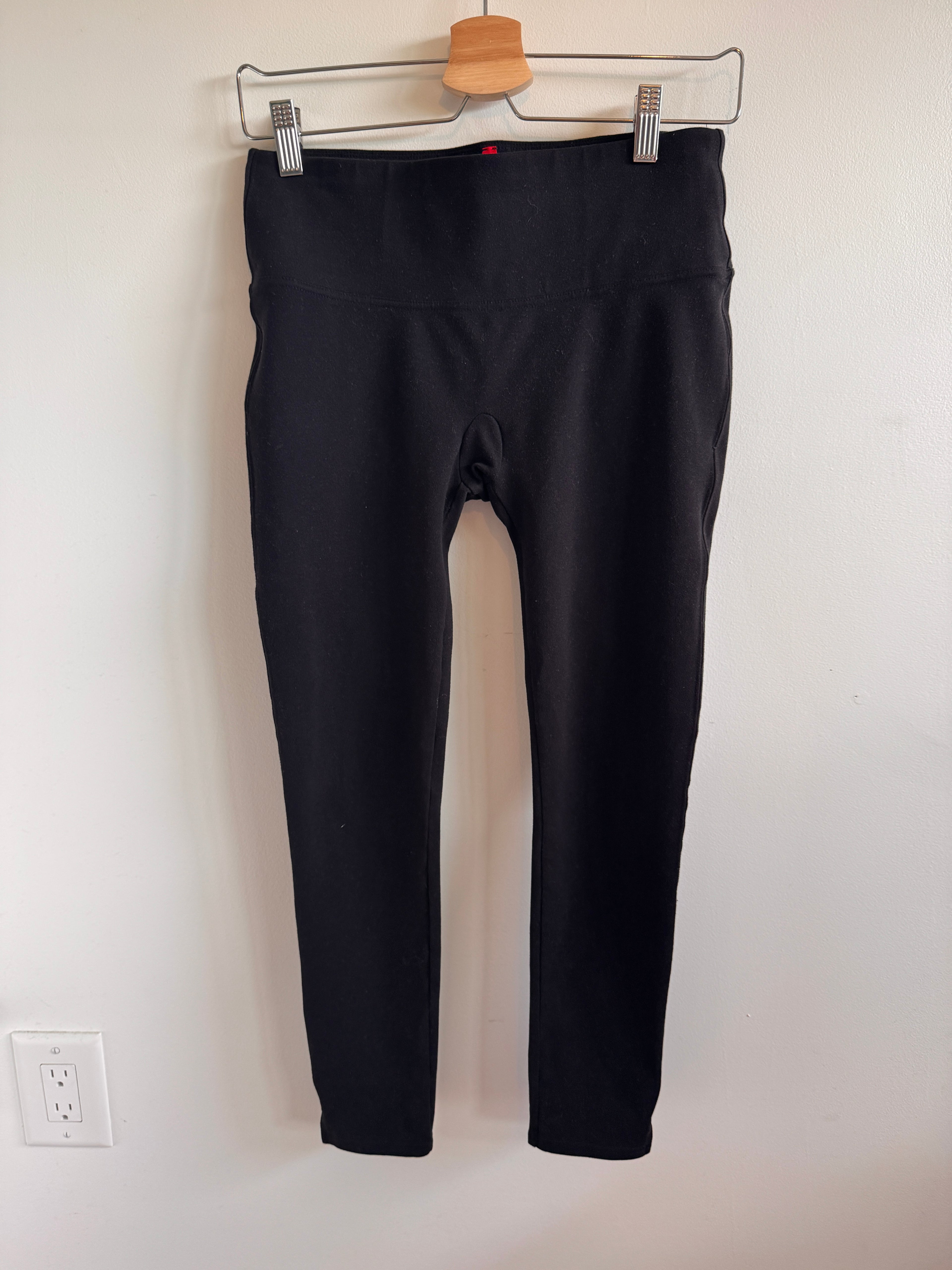 Black pants hanging on a white wall with a wooden hanger.