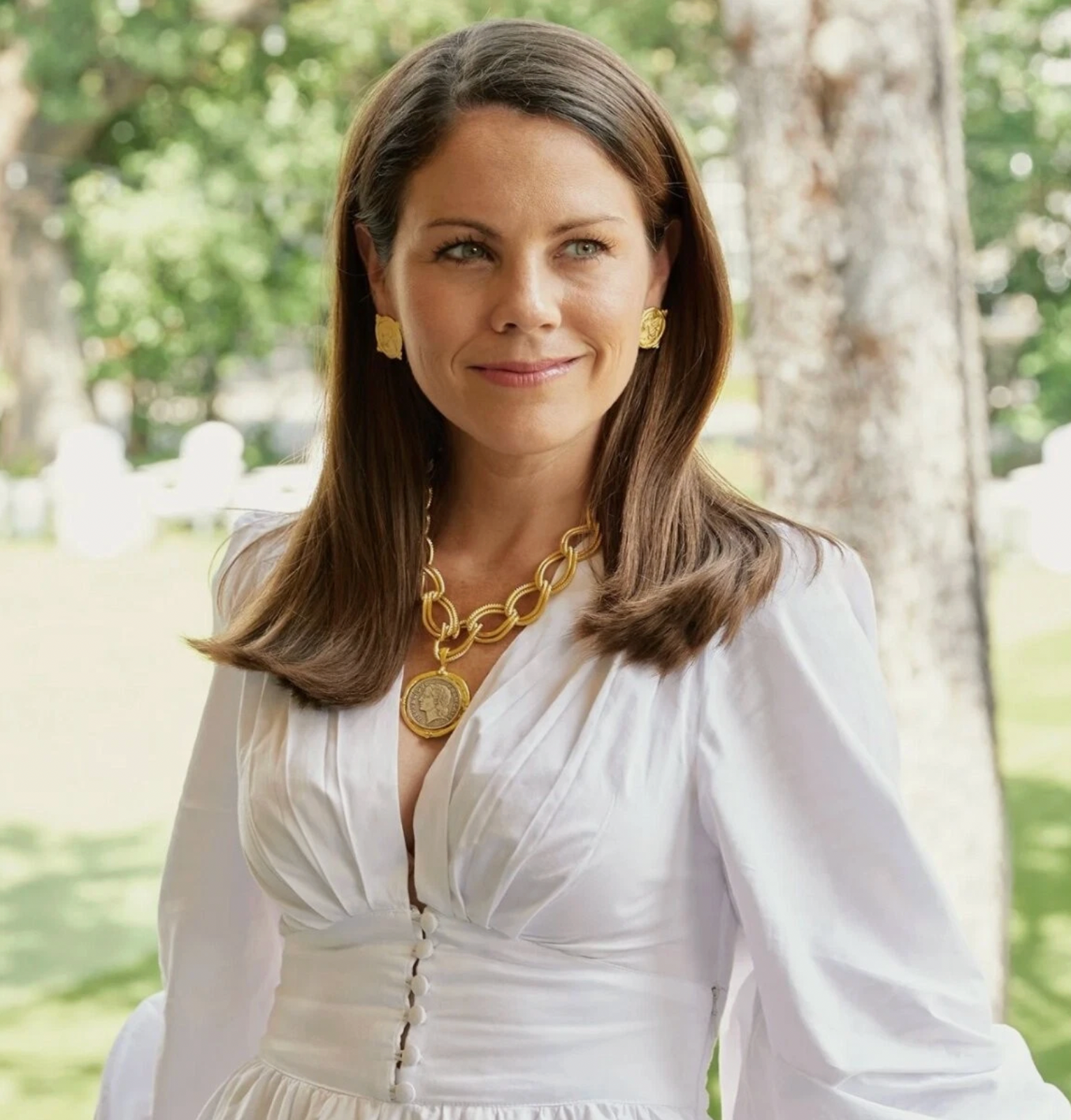 Woman wearing a white dress with gold jewelry in a park setting