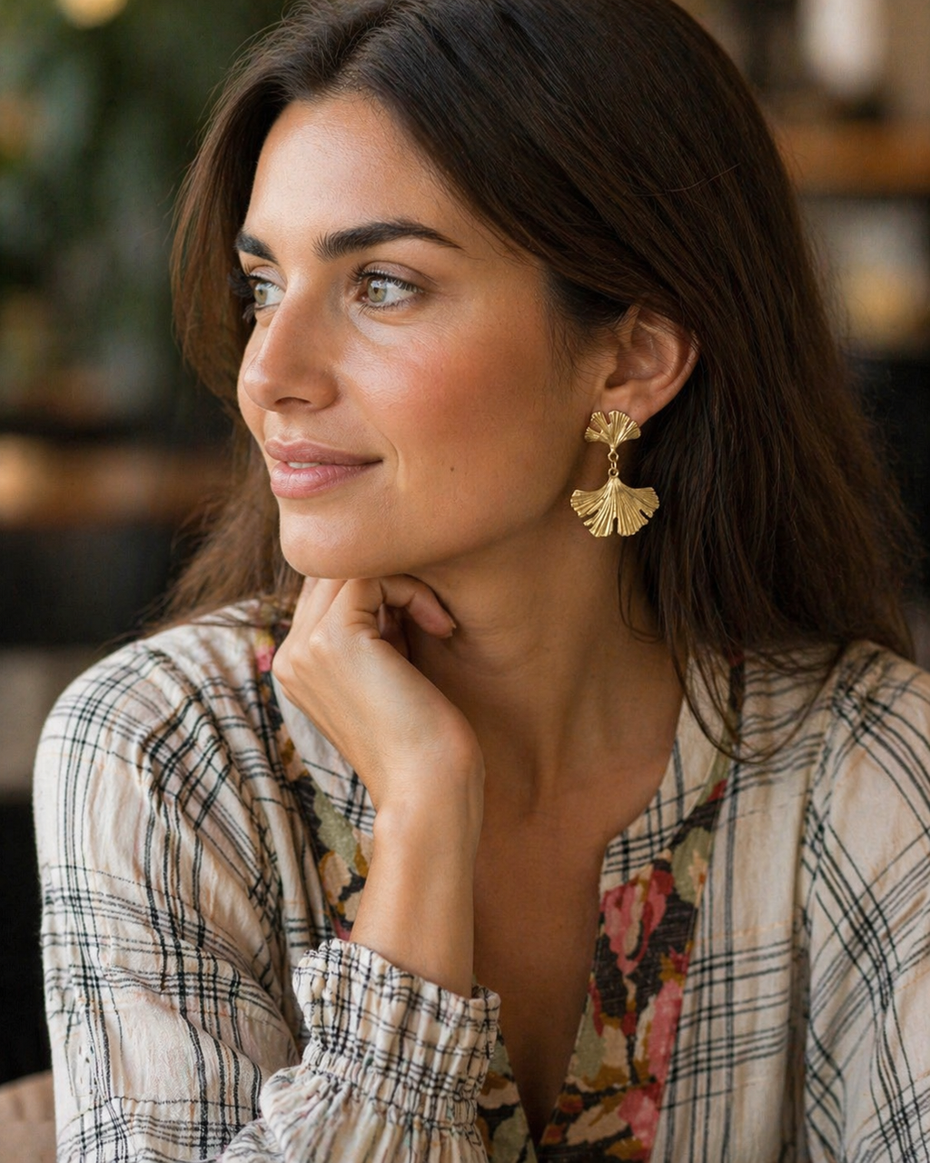 Woman wearing gold earrings with a blurred indoor background