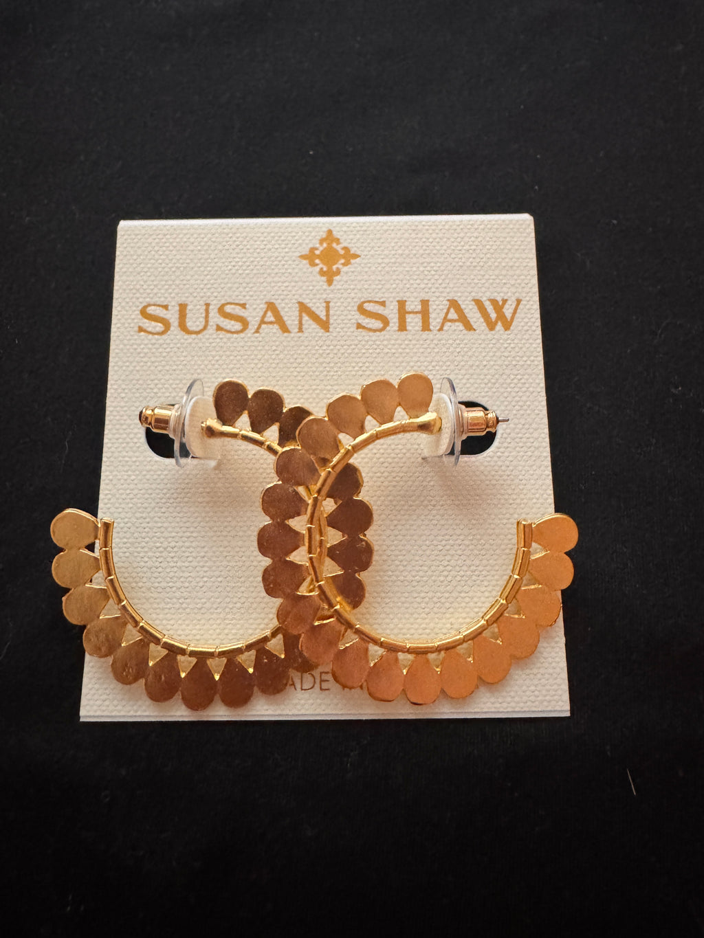 Gold-tone hoop earrings with scalloped disc detailing, displayed on a white Susan Shaw brand card against a black background.
