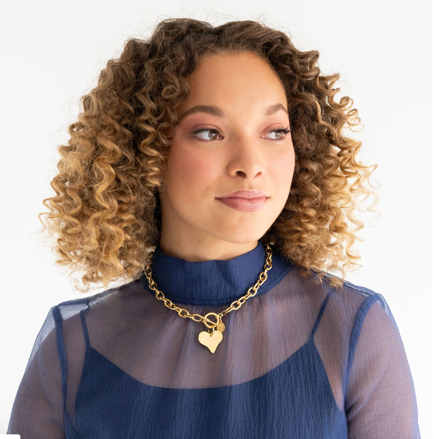 Woman wearing a gold necklace with a heart pendant on a white background