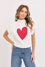 Woman wearing a white sweater with a red heart design on a plain background