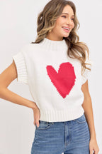 Woman wearing a white sweater with a red heart design on a plain background