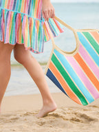 Person holding a colorful striped bag on a beach