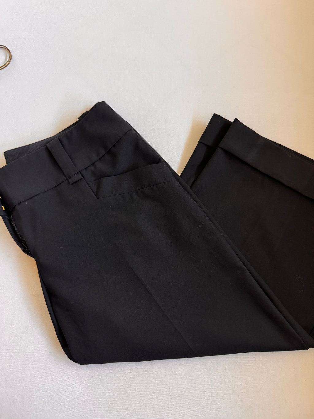 Folded pair of cropped black pants showing pockets and cuffs on a white background
