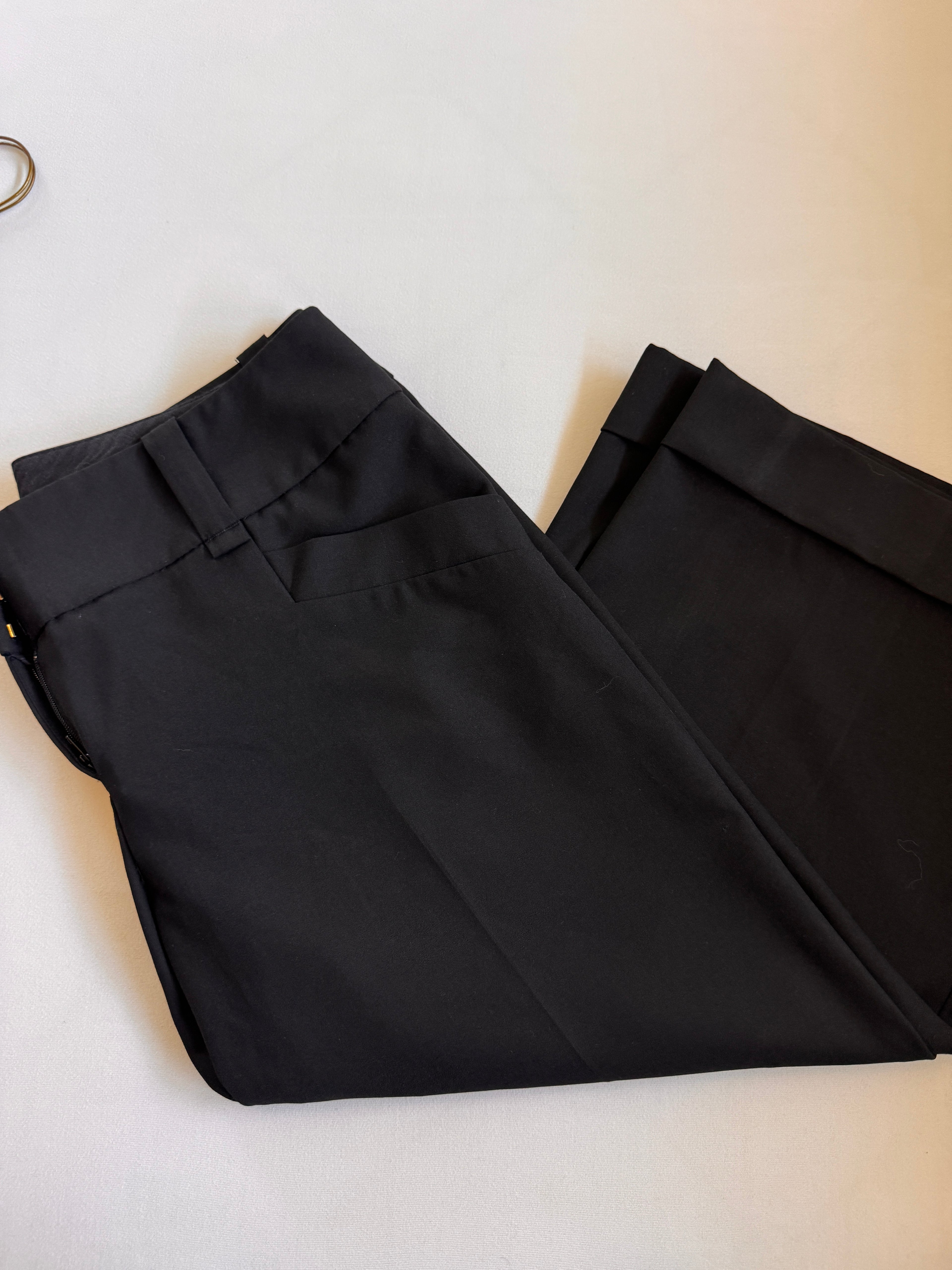 Folded pair of cropped black pants showing pockets and cuffs on a white background