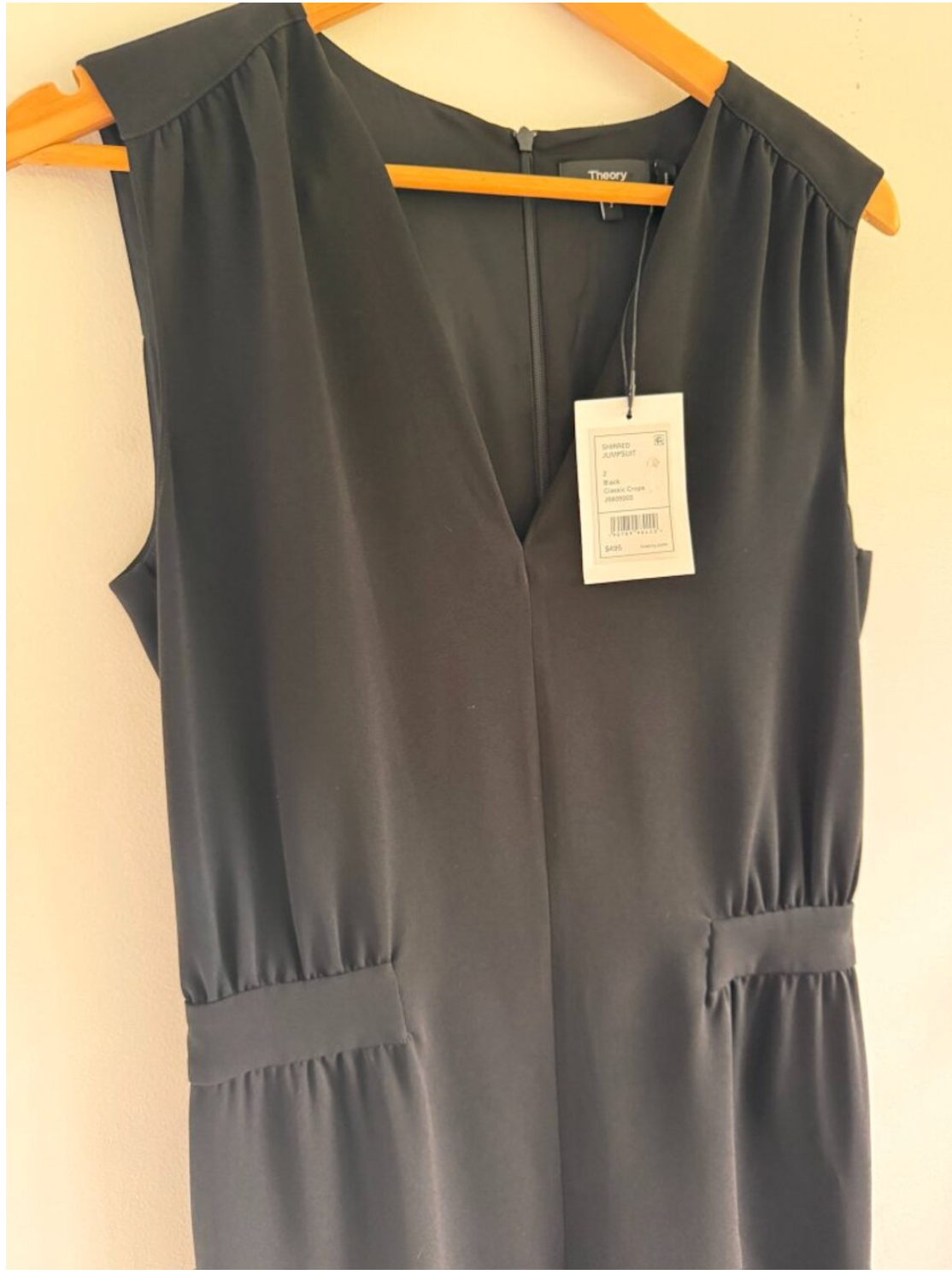 Gray sleeveless dress with a tag on a wooden hanger against a beige wall